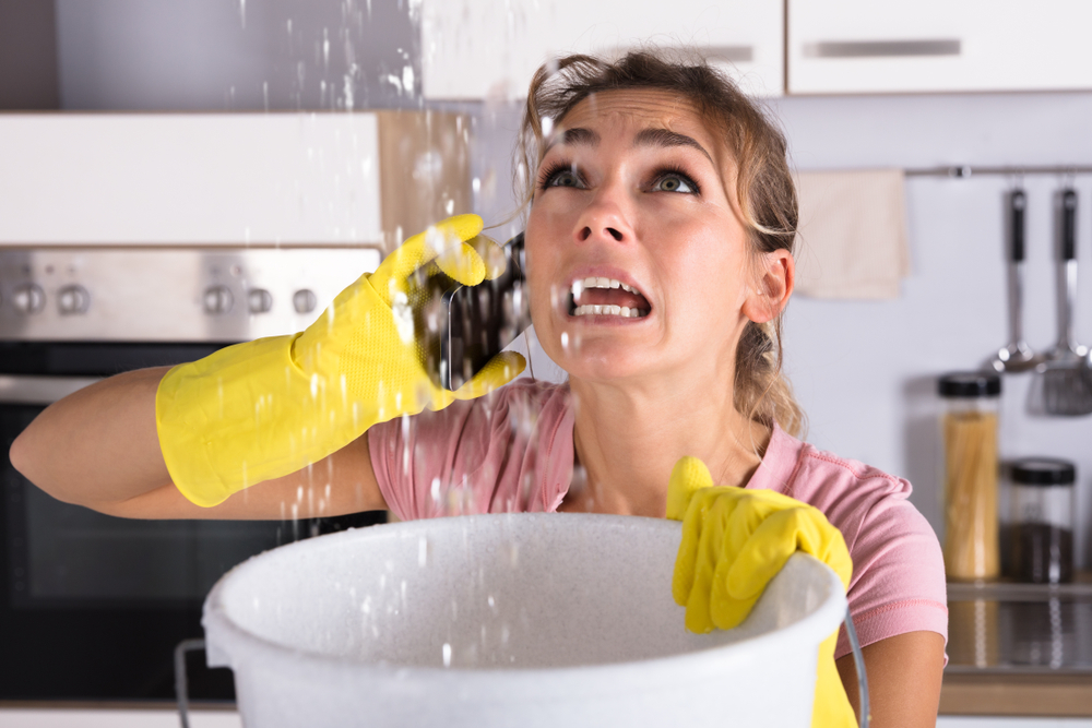 Woman Calling Plumber While Collecting Water Leaking From Ceiling
